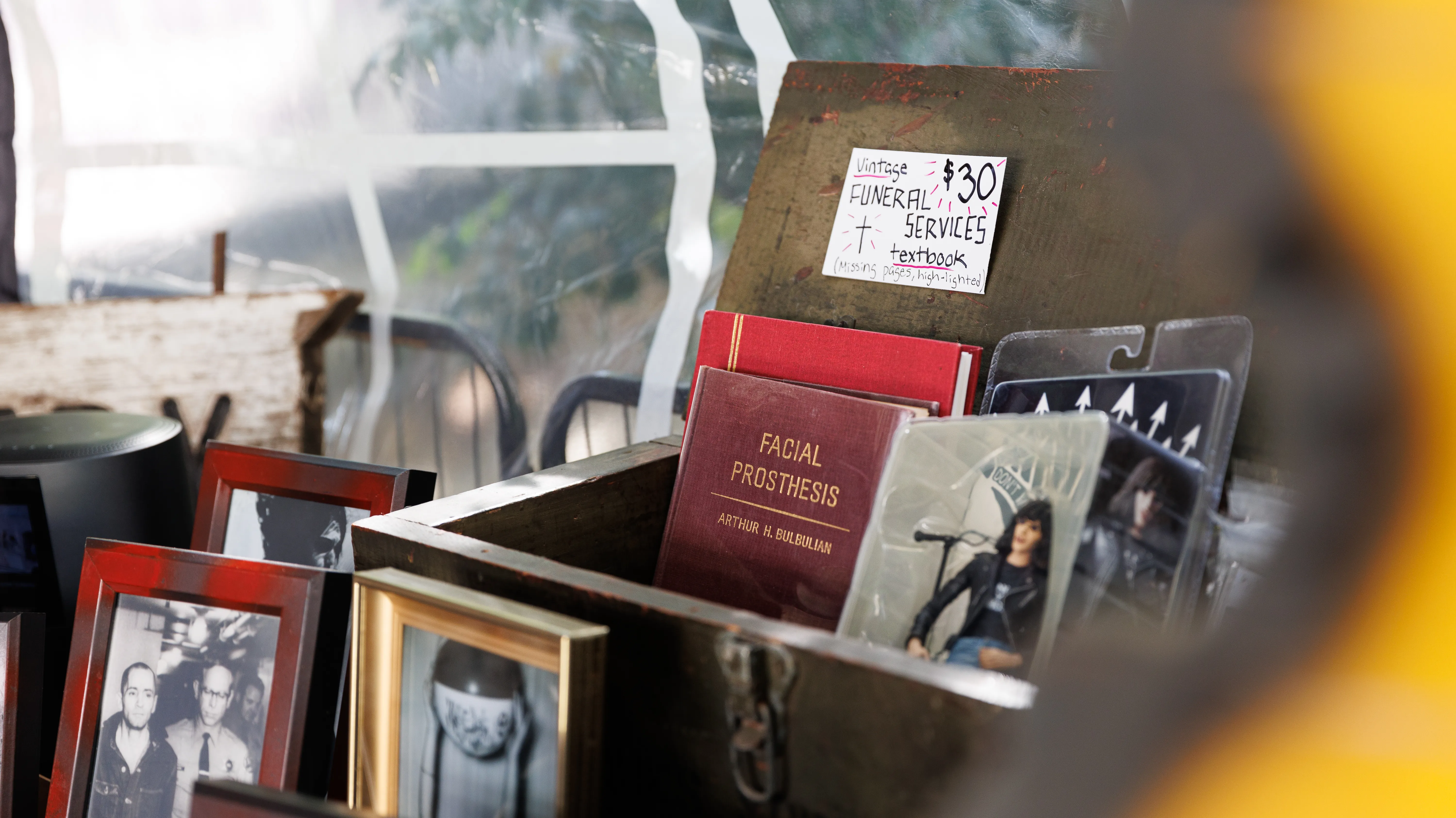 An old wooden box of curios, including a funeral services textbook, odd vintage photographs, and an old book on facial prothesis.