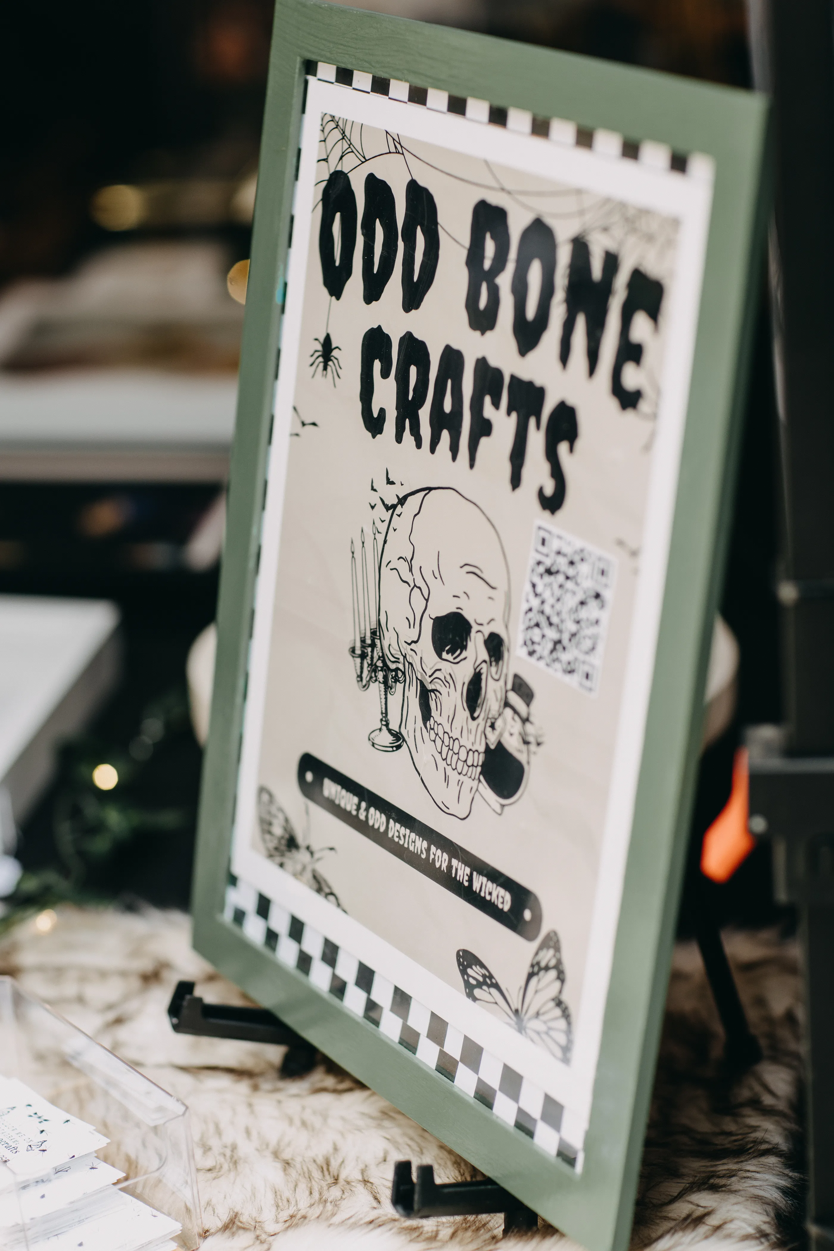 A vendor table sign that reads "Odd Bone Crafts - Unique and Odd Designs for the Wicked".