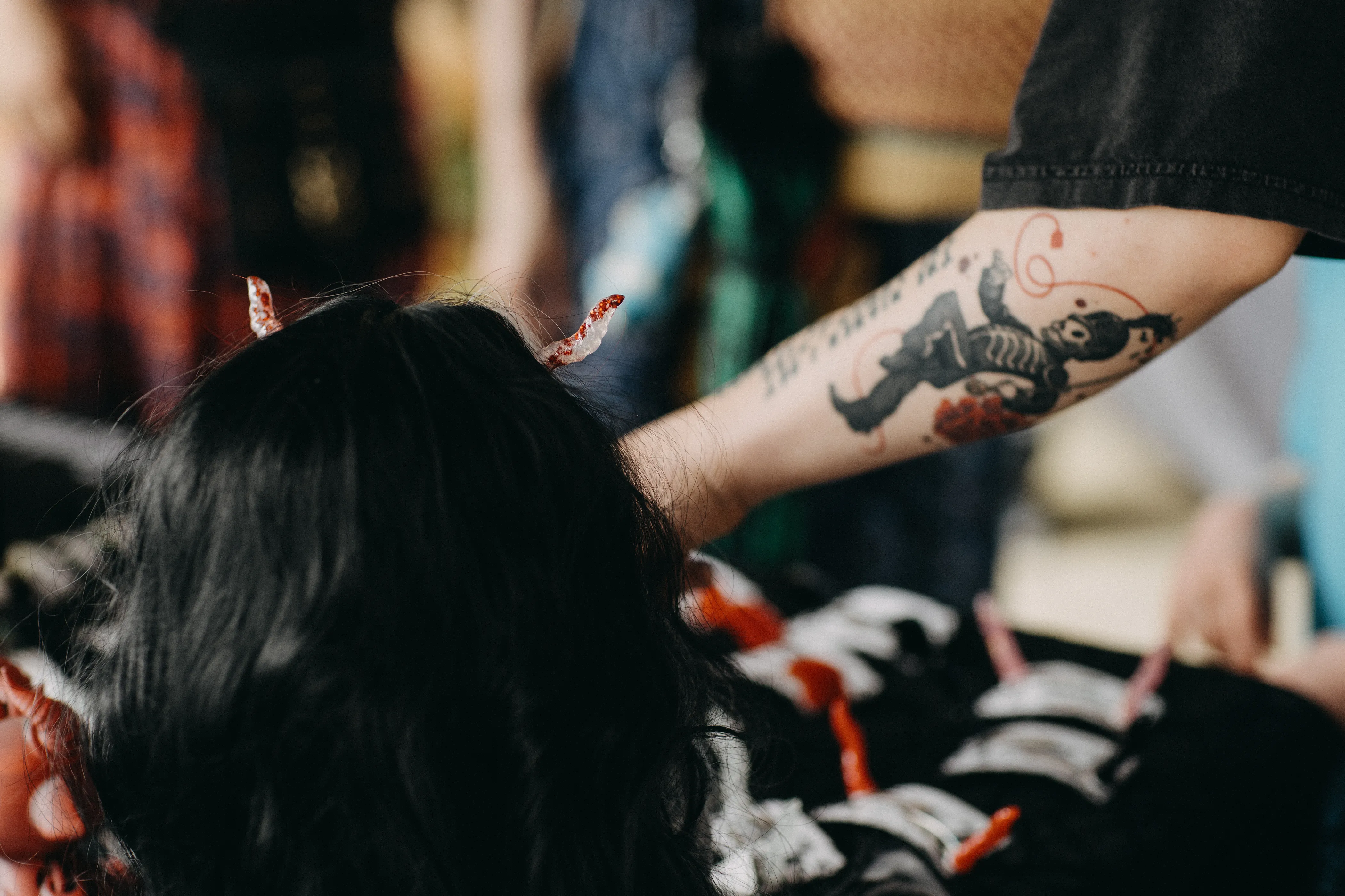 An arm in the background with a tattoo of an undead parade leader reaches for a table of prosthetic horns.