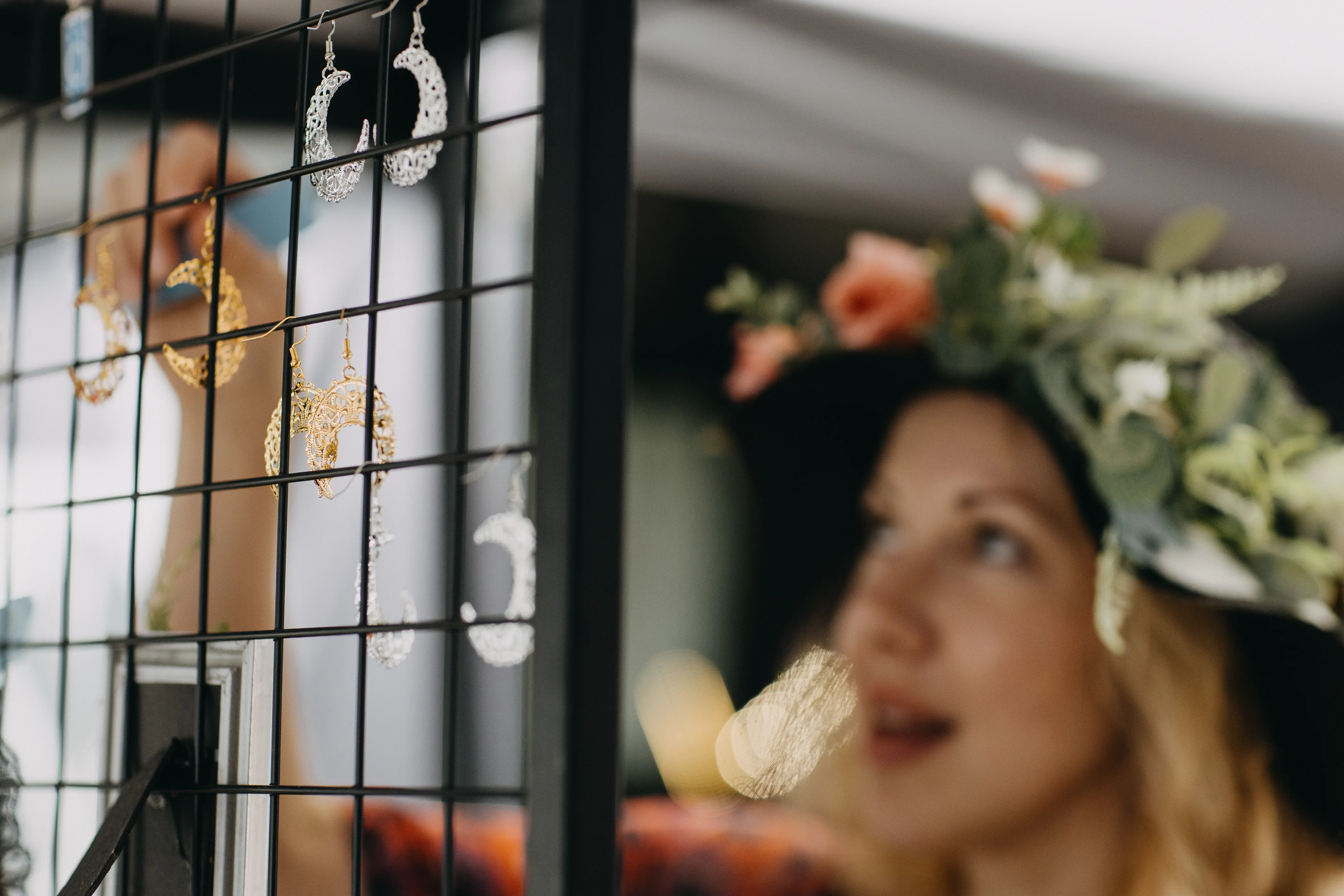 A customer in a floral adorned hat joyfully picking out local handmade earrings.